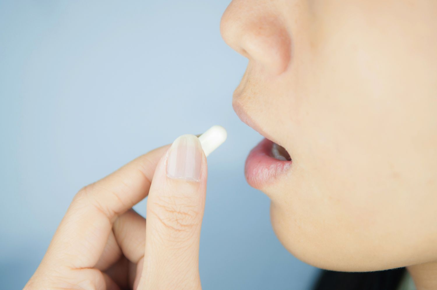  Eine Frau führt eine Tablette zu ihrem Mund. Thema: Frauenbeschwerden