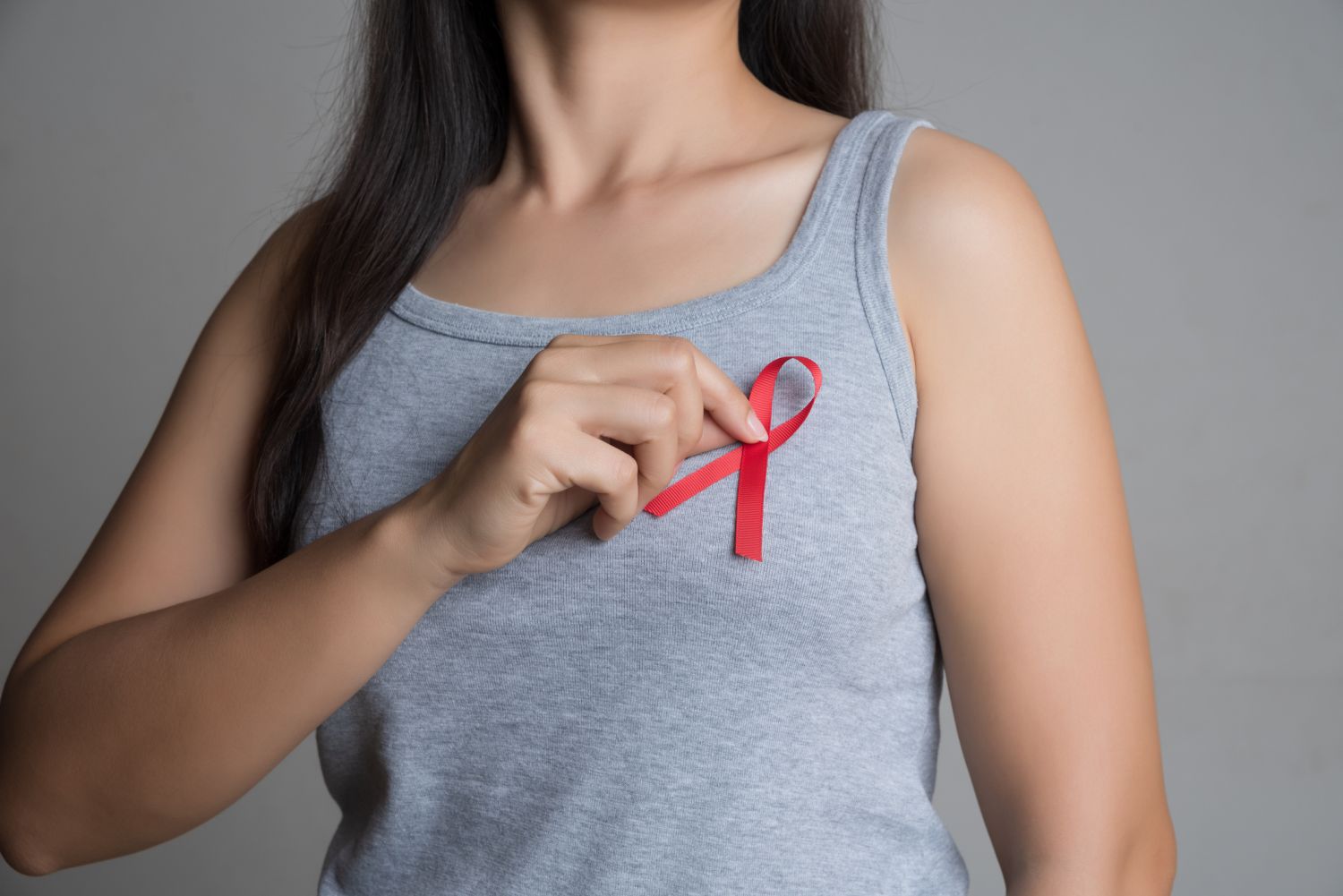 Eine Frau hält sich eine rote Schleife, die für Solidarität mit HIV-Infizierten steht, an ihre Brust.