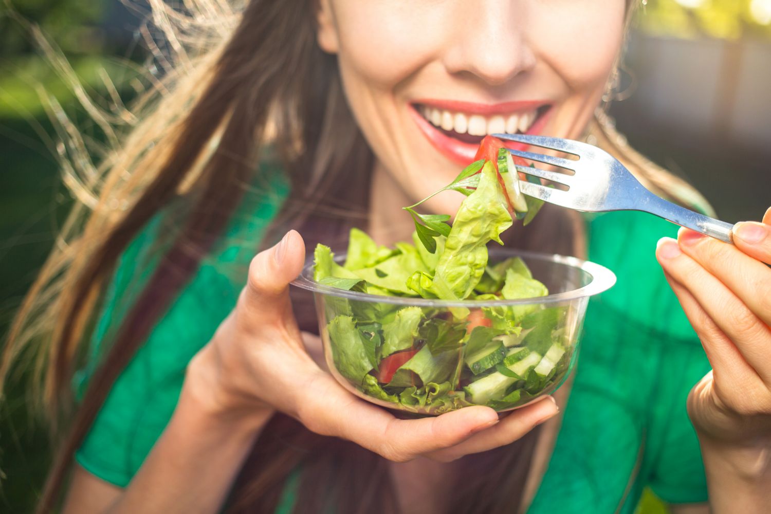Lachende Frau isst Salat aus Schale in der Hand. Thema: Mentale Gesundheit