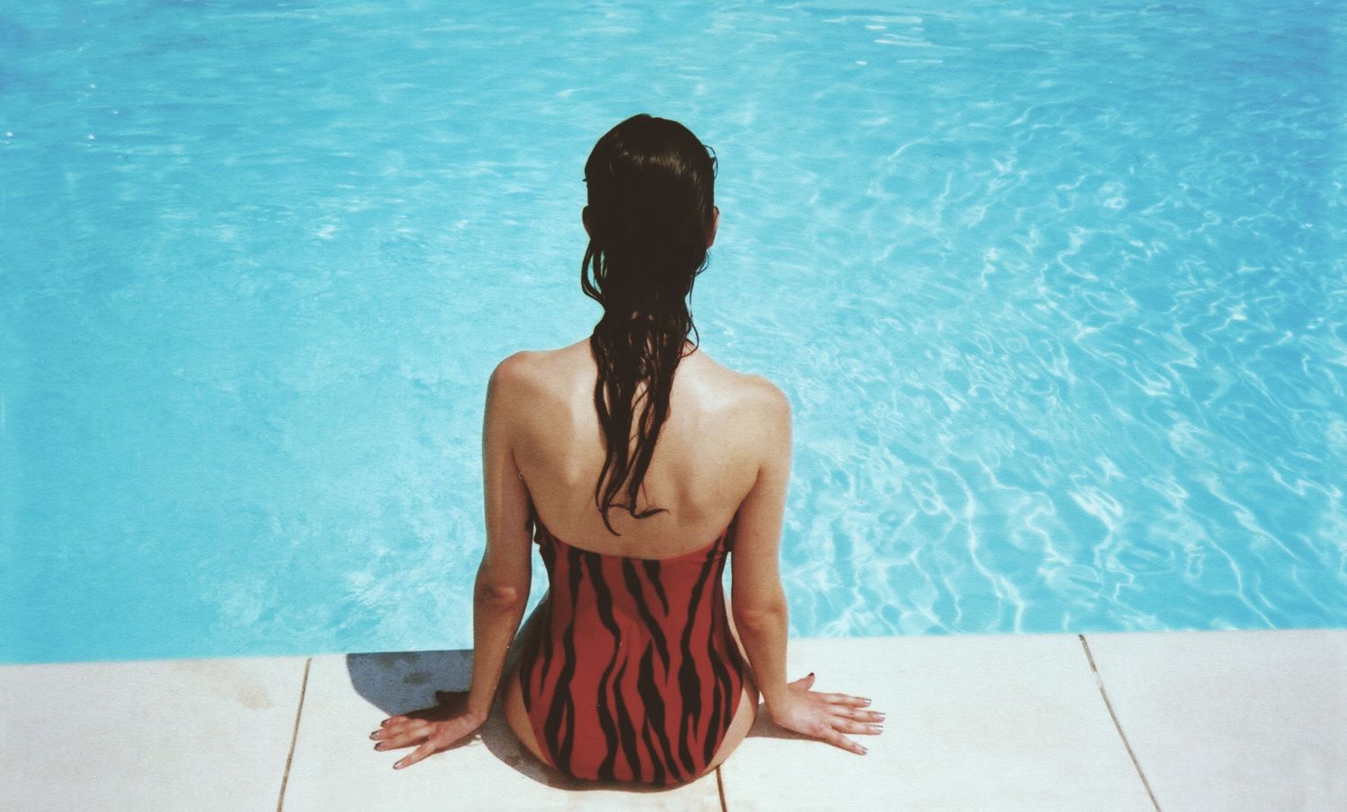  Eine Frau sitzt im Bikini am Pool. Thema: Frauengesundheit