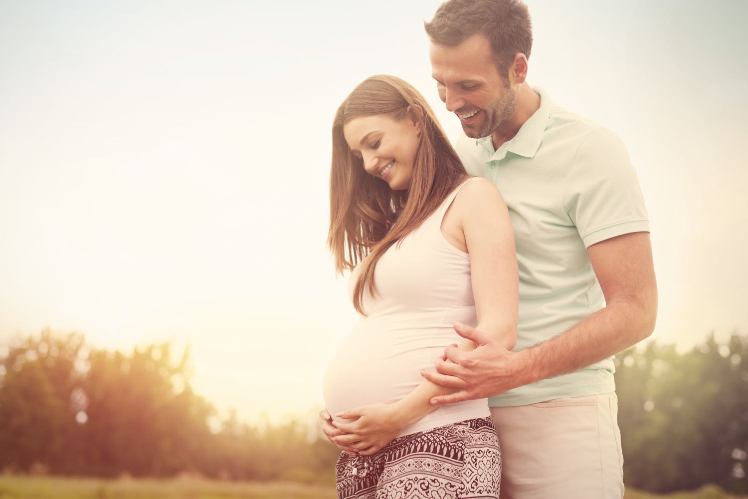 Eine schwangere Frau wird von ihrem Partner umarmt. Thema: staatliche Zuschüsse künstliche Befruchtung